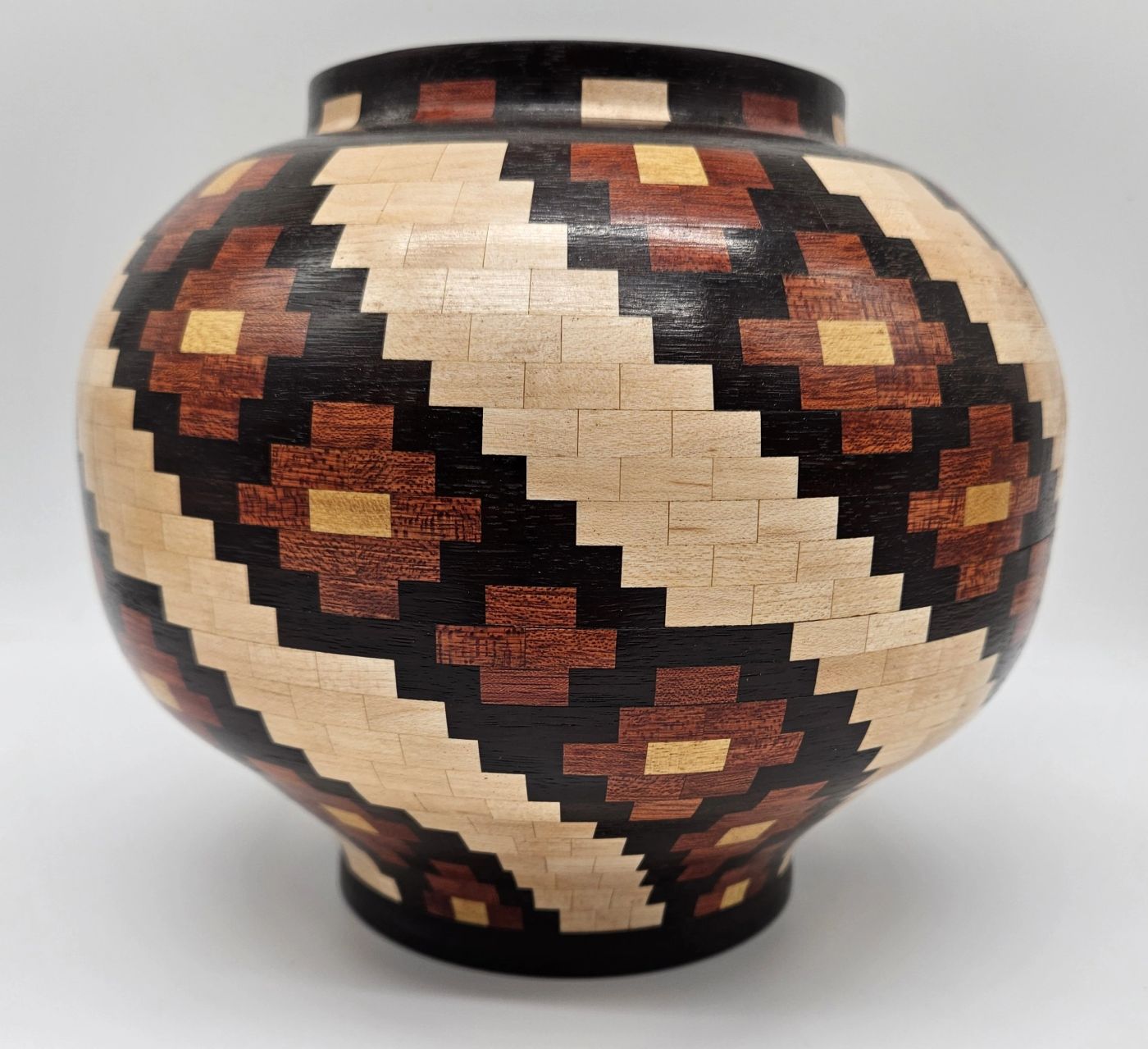 Rounded segmented wooden jar covered in a diagonal stepped diamond pattern of pale maple, red-brown and dark hardwood
