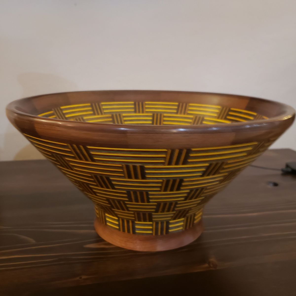 A flared wooden bowl with a walnut rim and a body patterned to look like woven basketry in gold and dark brown