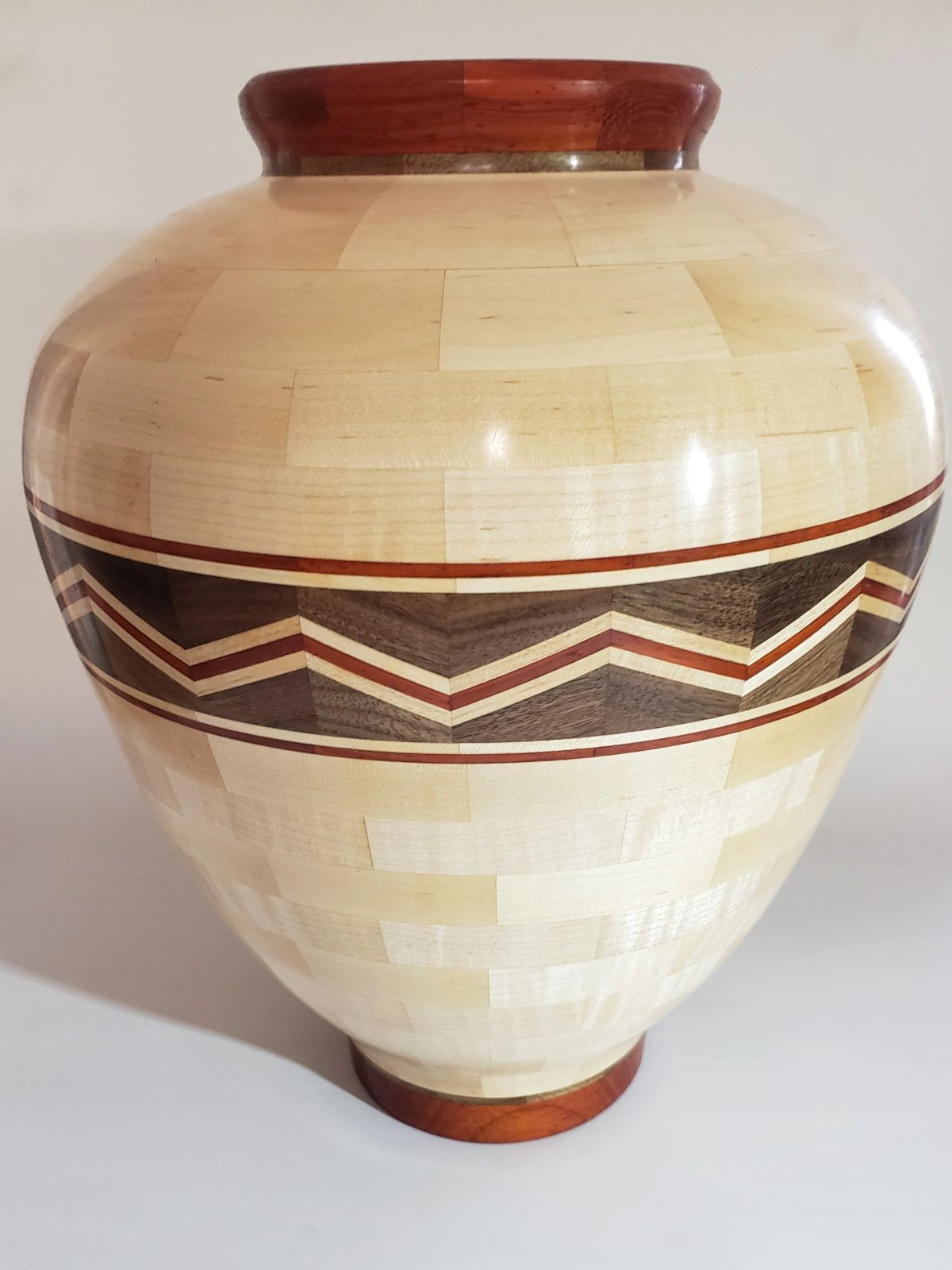 A tall segmented wooden jar in pale maple with a chevron band of walnut and padauk around its widest point