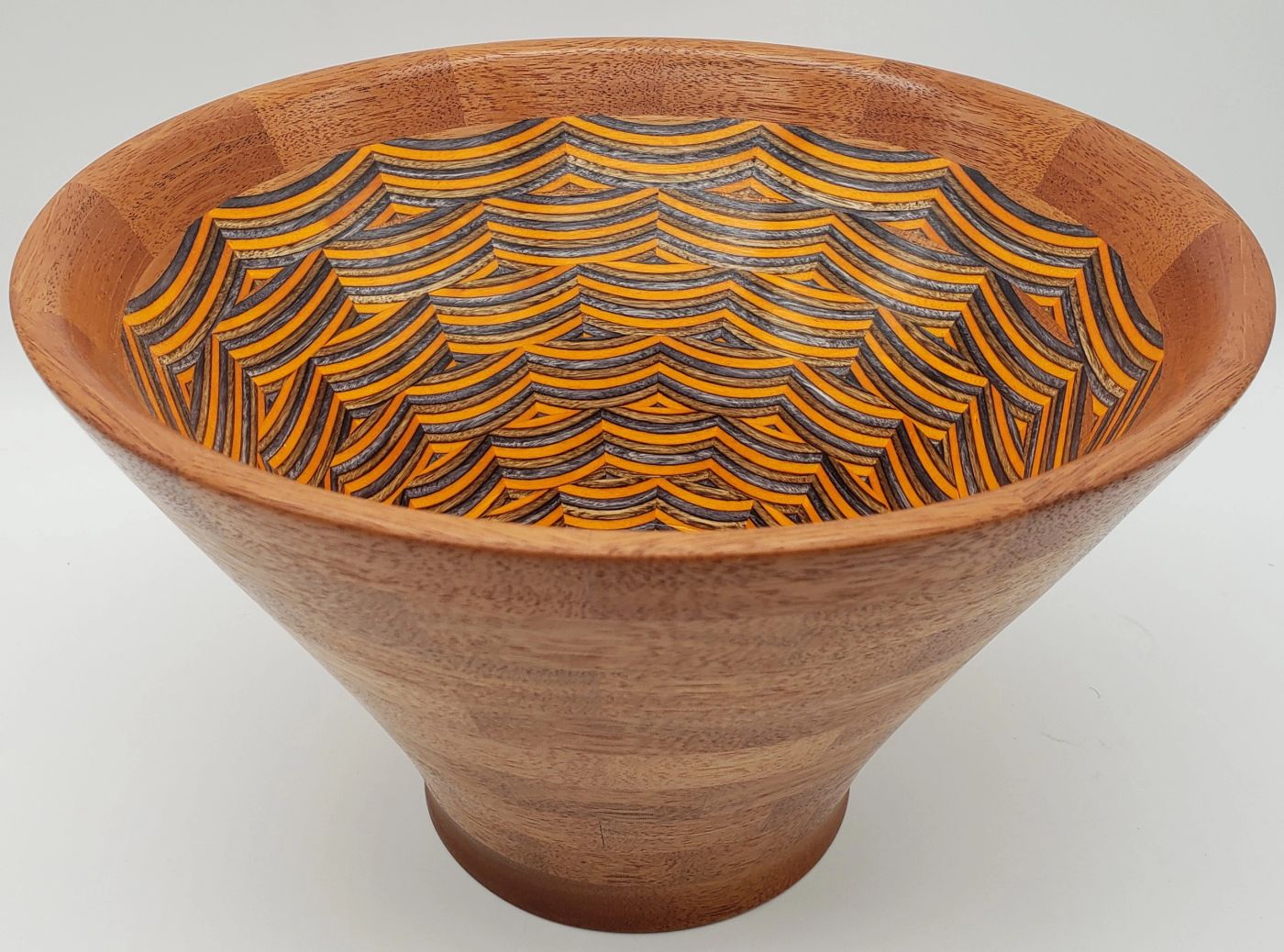Wide conical wooden bowl in warm mahogany opening onto an interior of overlapping orange, grey and cream scalloped arcs