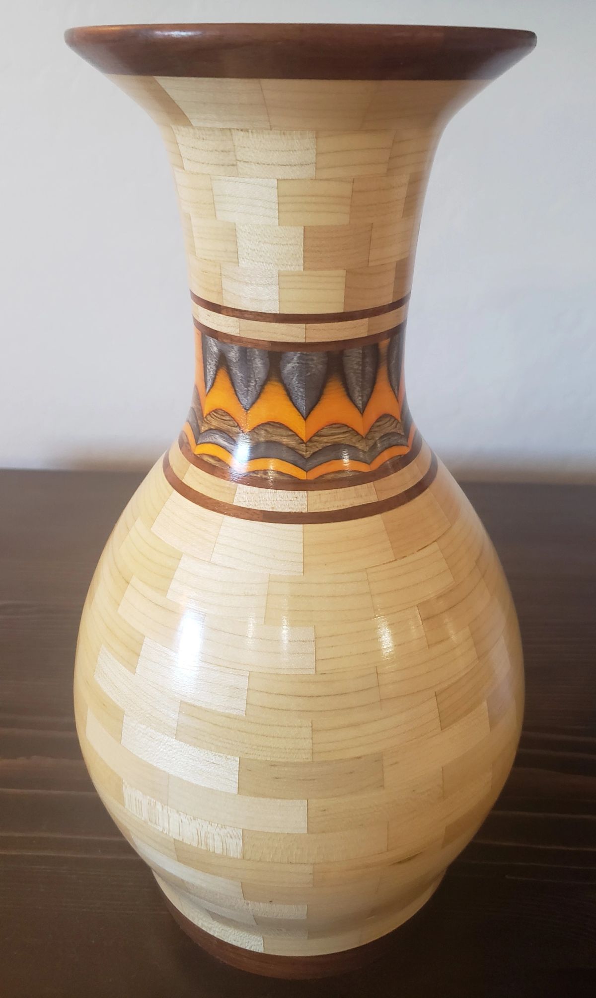 A tall segmented wooden vase in pale maple with a flared rim and a narrow feature band of orange and grey around the neck