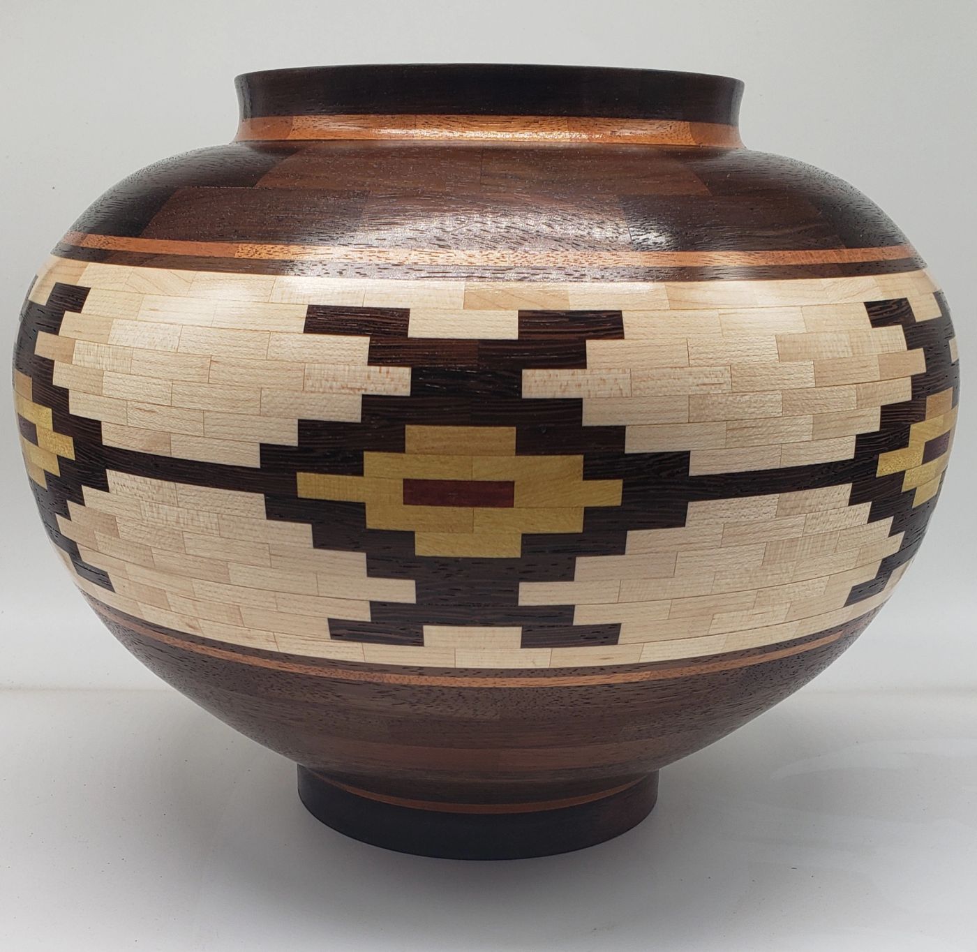 Wide segmented wooden vessel with a pale maple band holding a stepped geometric motif in dark brown, gold and red